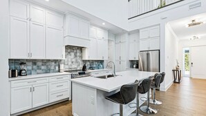 A modern kitchen with white cabinetry, a large island with bar stools, a stainless steel refrigerator, and a tiled backsplash.