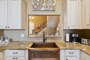 A kitchen with a granite countertop, a copper sink, white cabinetry, a coffee maker, and a toaster.