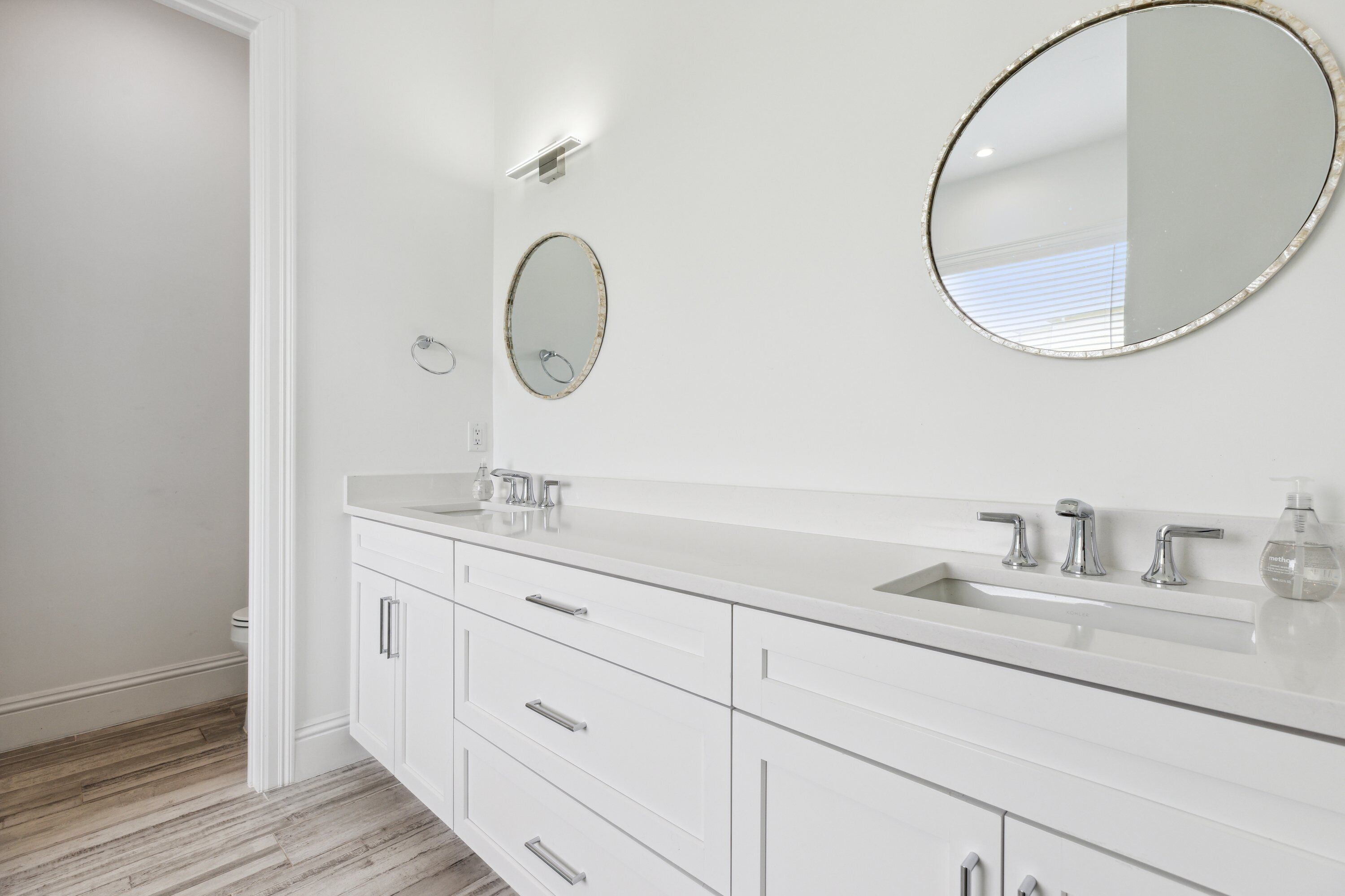 A modern bathroom with a white vanity, two sinks, and a large mirror.