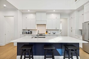 A modern kitchen with white cabinets, a large island with stools, and a stainless steel refrigerator.