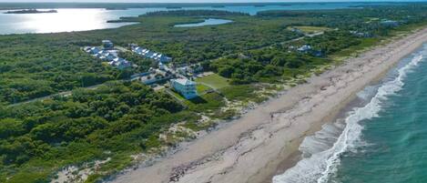 An aerial view of a coastal area with a beach, a cluster of buildings, and a large body of water.