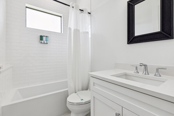 A modern bathroom with a white bathtub, a toilet, and a sink with a mirror above it. - 119 Ocean Estates Dr (Fort Pierce)