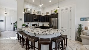 A modern kitchen with dark cabinets, a large island with bar stools, stainless steel appliances, and pendant lighting. - 106 Mediterranean Way (Indian Harbour Beach)