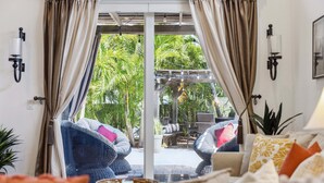 A room with a sliding glass door leading to an outdoor area with chairs and a table, a bed with pillows, and wall-mounted lights. - 106 Mediterranean Way (Indian Harbour Beach)