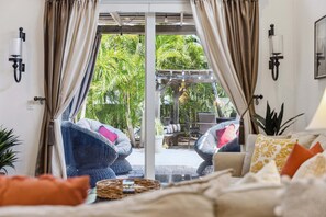 Quarto com porta de vidro deslizante para área externa com cadeiras e mesa, cama com almofadas e luminárias fixadas na parede.