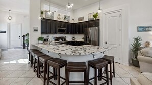 A modern kitchen with dark cabinets, a large island with stools, stainless steel appliances, and pendant lighting. - 106 Mediterranean Way (Indian Harbour Beach)