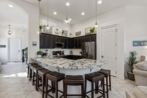Uma cozinha moderna com armários escuros, uma ilha grande com banquetas, eletrodomésticos de aço inoxidável e iluminação pendente.
