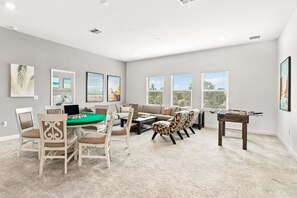 A spacious living room with a green table, comfortable seating, a foosball table, and large windows. - 390 Strand Drive (Melbourne Beach)