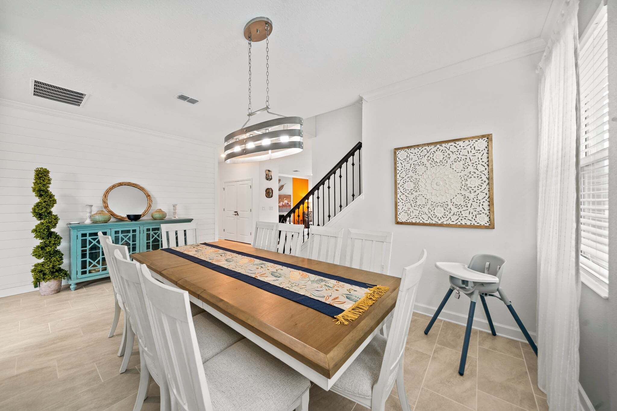 Un comedor con una mesa de madera, sillas blancas, un armario azul verdoso y una escalera.