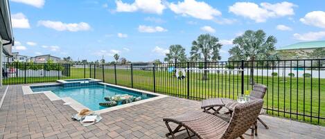 A pool area with lounge chairs, a brick patio, and a view of the surrounding landscape.