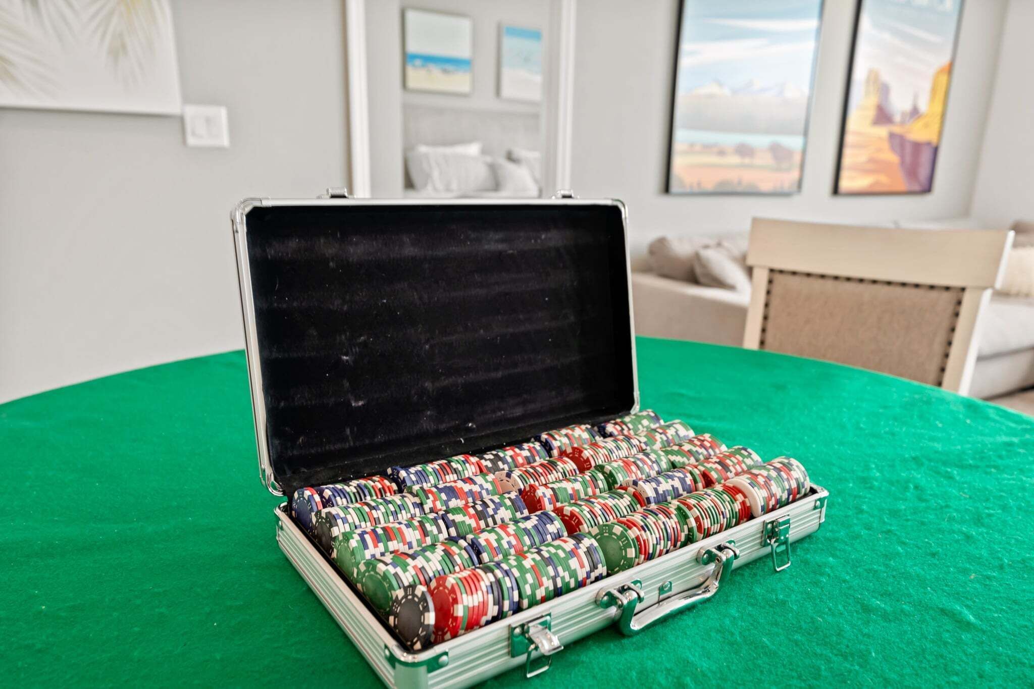 A poker chip case on a green table in a room with a couch and framed pictures on the wall.
