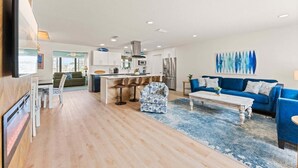 A modern living room with a blue sofa, a coffee table, and a kitchen area with a dining table and bar stools. - 384 Harbor Drive (Cape Canaveral)
