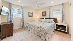 A bedroom with a bed, a nightstand, a dresser, a ceiling fan, and two windows with curtains. - 384 Harbor Drive (Cape Canaveral)