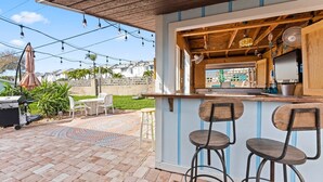 An outdoor bar area with a wooden counter, two stools, and string lights. - 384 Harbor Drive (Cape Canaveral)