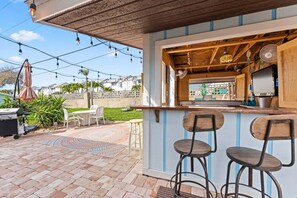 An outdoor bar area with a wooden counter, two stools, and a grill.
