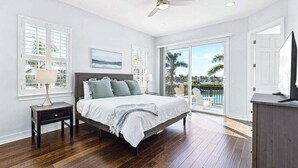 A bedroom with a bed, a nightstand, a ceiling fan, and a view of the outdoors through a sliding glass door. - 136 Mediterranean Way (Indian Harbour Beach)