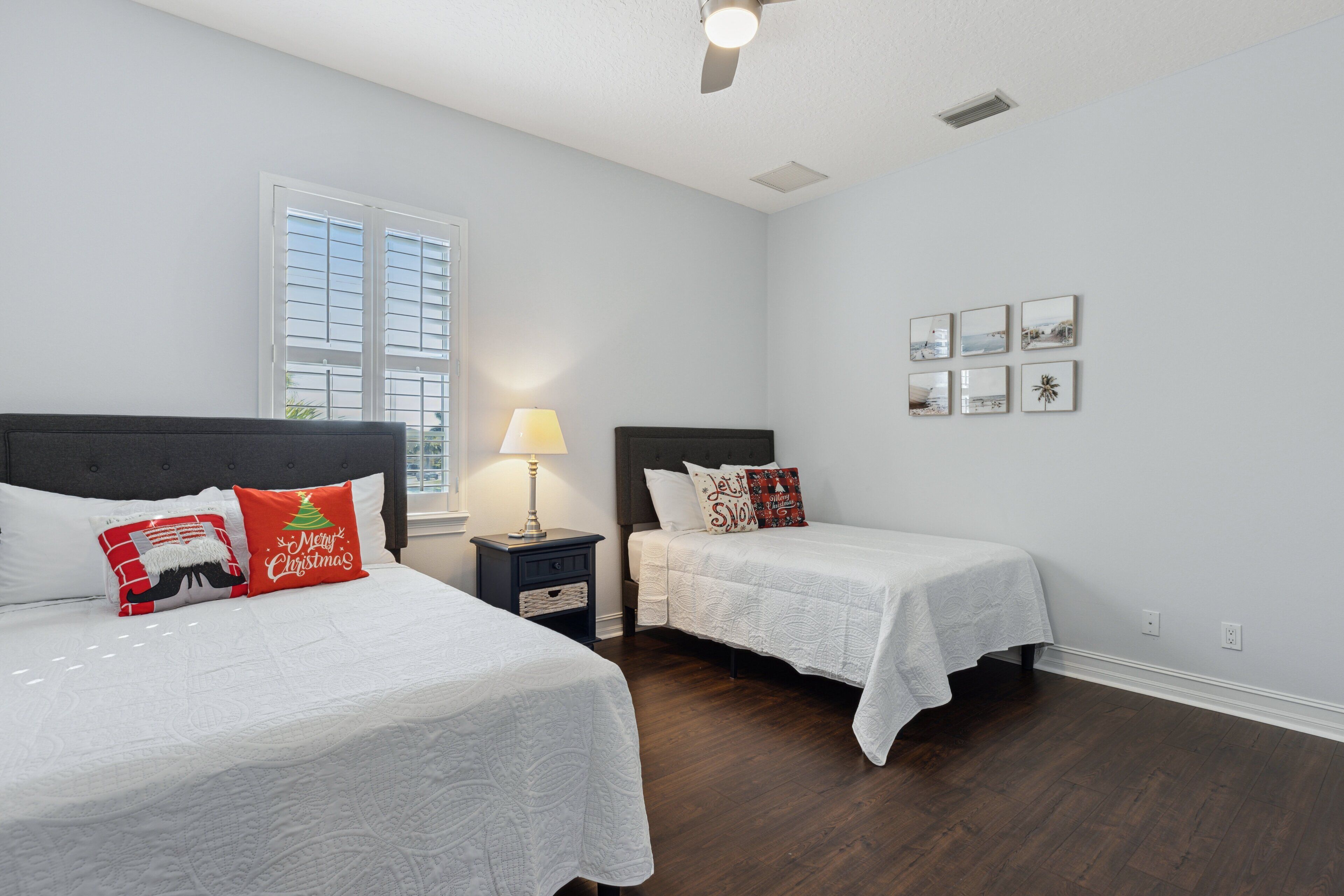 A bedroom with two beds, a window, a ceiling fan, and wall art.