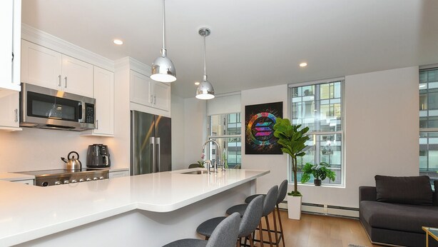 Een moderne keuken met een centraal eiland, roestvrijstalen apparatuur en barstoelen.