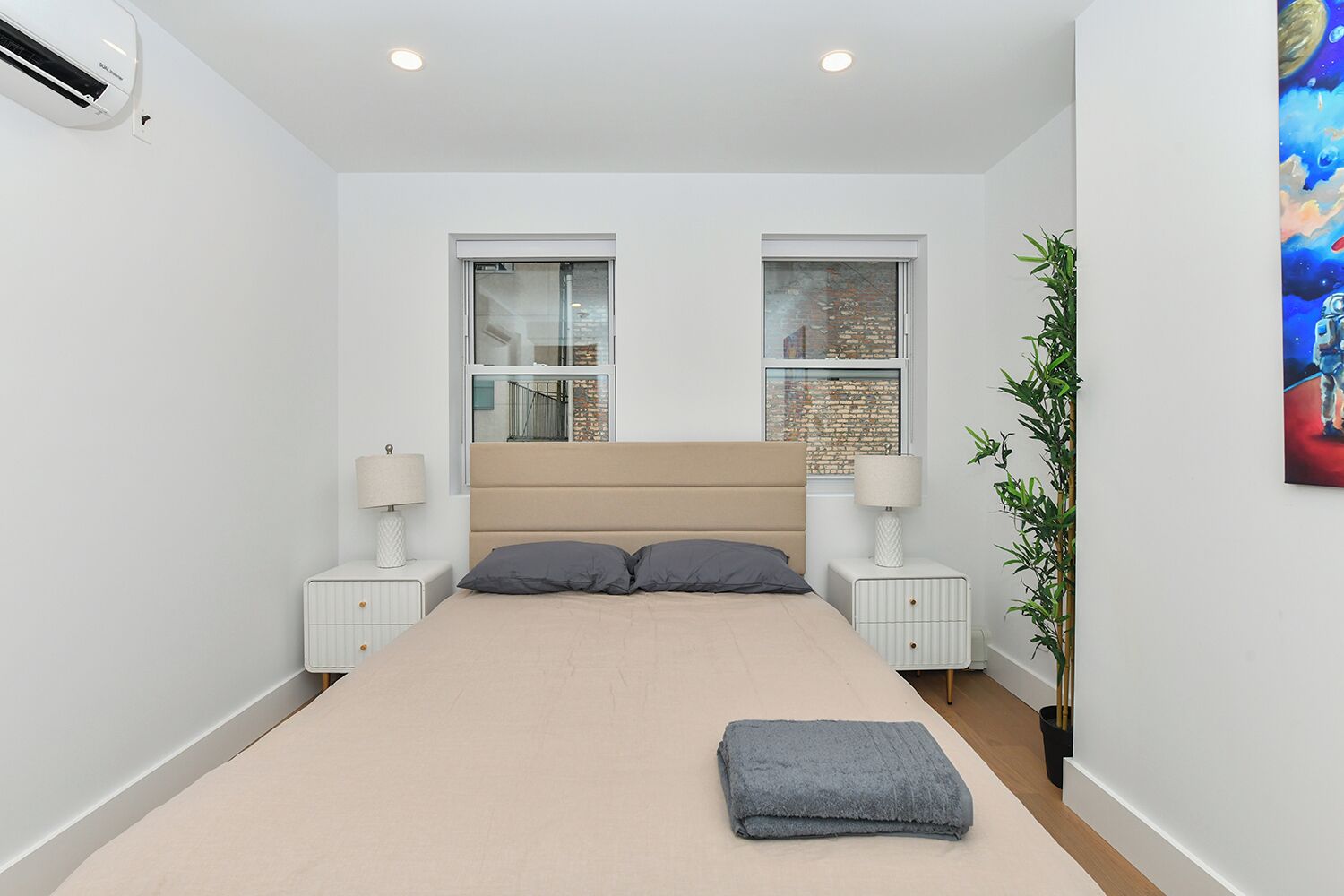 A bedroom with a bed, two bedside tables with lamps, a window, and a plant.