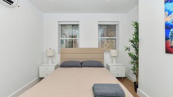 A bedroom with a bed, two bedside tables with lamps, a window, and a plant.