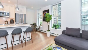 Een modern appartement met keuken, eetgedeelte en woonkamer. Het heeft een groot raam met uitzicht op de stad, een bank en een salontafel.