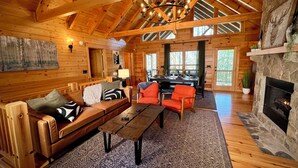 Un intérieur spacieux de chalet en bois, avec un plafond en bois, une cheminée en pierre, un coin repas et un espace salon confortable.