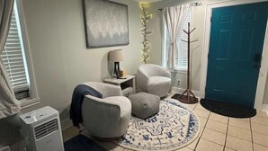 Un salon avec deux fauteuils, une petite table, une lampe, une plante décorative et une porte bleue.