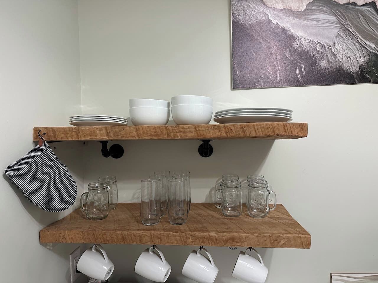 Dos estantes de madera con cuencos blancos, platos y tazas de vidrio transparente.