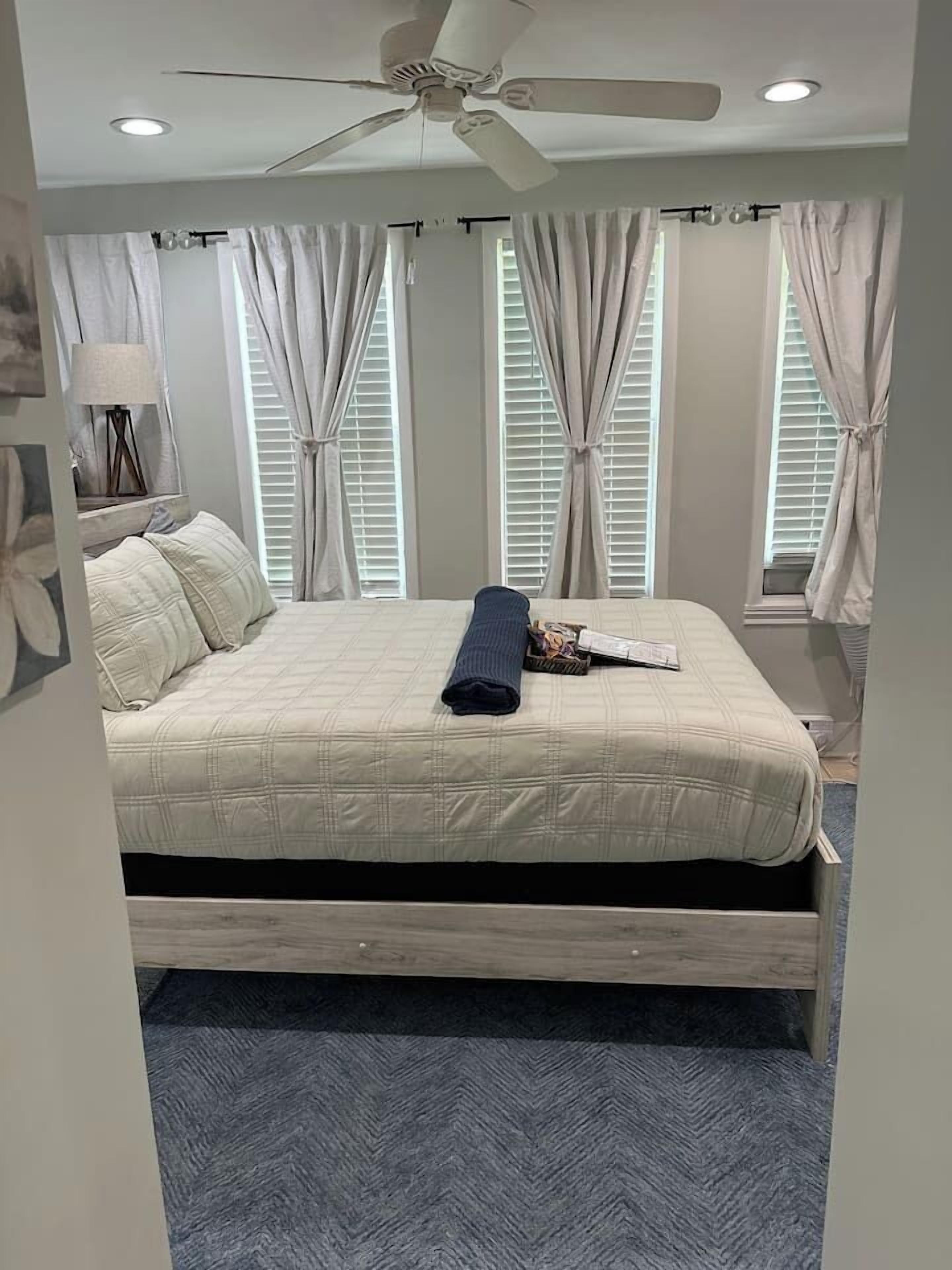 A bedroom with a bed, a ceiling fan, and windows with curtains.