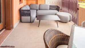 Ein überdachter Patio-Bereich mit einer Eckcouch, Korbstühlen und einem Fliesenboden.