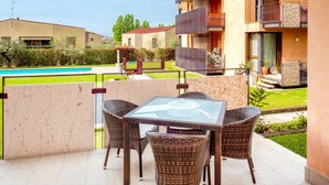 Eine Terrasse mit Glastisch und Korbstühlen, mit Blick auf einen Pool und einen Garten.
