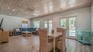 A spacious living room with a wooden ceiling, a blue sofa, wicker chairs, a dining table, and a view of a swimming pool through large windows. - NEW LISTING!!! QUIT 'N TIME - 5BD, LRG PRIV POOL & PATIO, WLK TO SEASIDE & BEACH (Santa Rosa Beach)