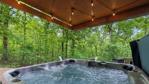 Un bain à remous situé dans un espace boisé, avec une terrasse en bois et une vue sur les arbres environnants.