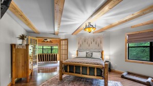A bedroom with a wooden bed, a patterned rug, a wooden dresser, and a window with a view of greenery.