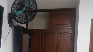 A room with a wooden wardrobe, a black cabinet, and a standing fan. - Hotel Los Arcangeles (San Jose de Cucuta)