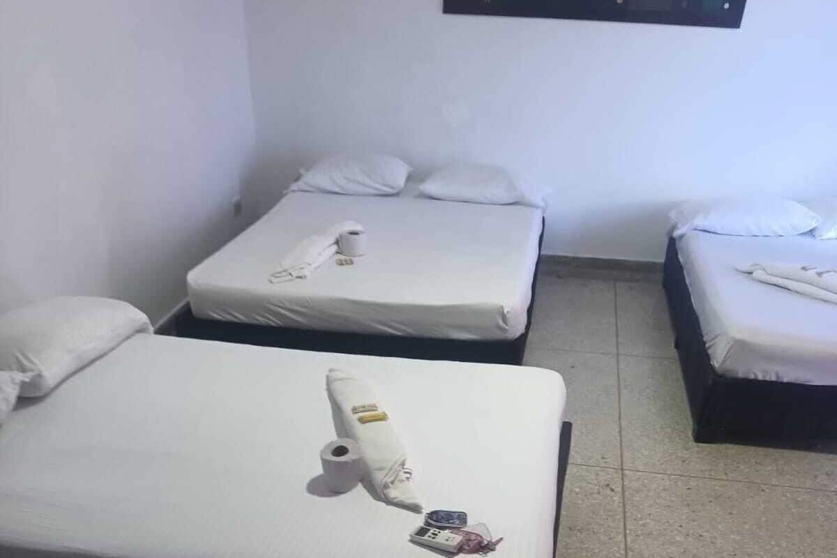 Ein kleines, sauberes Zimmer mit drei Einzelbetten, jeweils mit weißer Bettwäsche und Kissen.