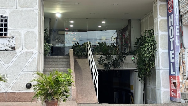 A hotel entrance with a stone facade, a staircase leading to the upper floor, and a sign indicating 24-hour service. - Hotel Los Arcangeles (San Jose de Cucuta)