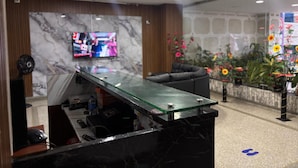 A reception area with a marble wall, a television, a sofa, and a flower arrangement. - Hotel Los Arcangeles (San Jose de Cucuta)