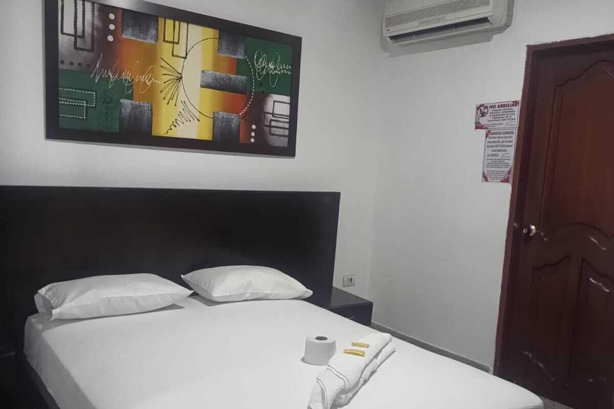 Ein Hotelzimmer mit Bett, weißen Bettwäsche, einem Nachttisch, einer Wandklimaanlage und einer Tür.