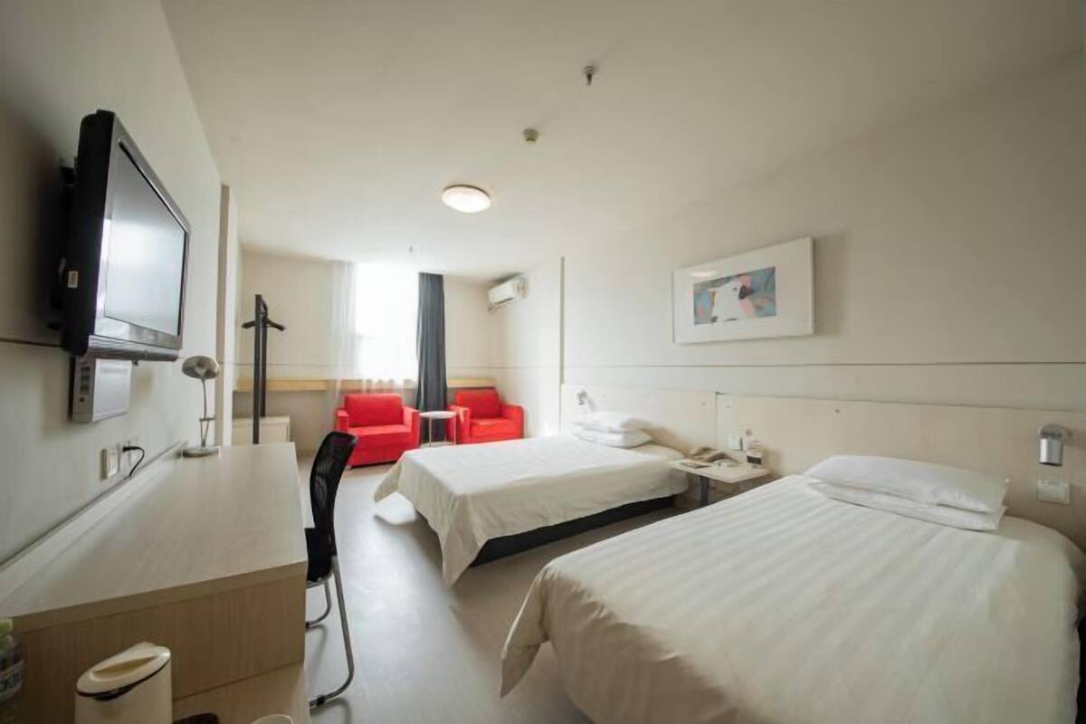 Habitación de hotel con dos camas, un escritorio, un televisor y una silla roja.