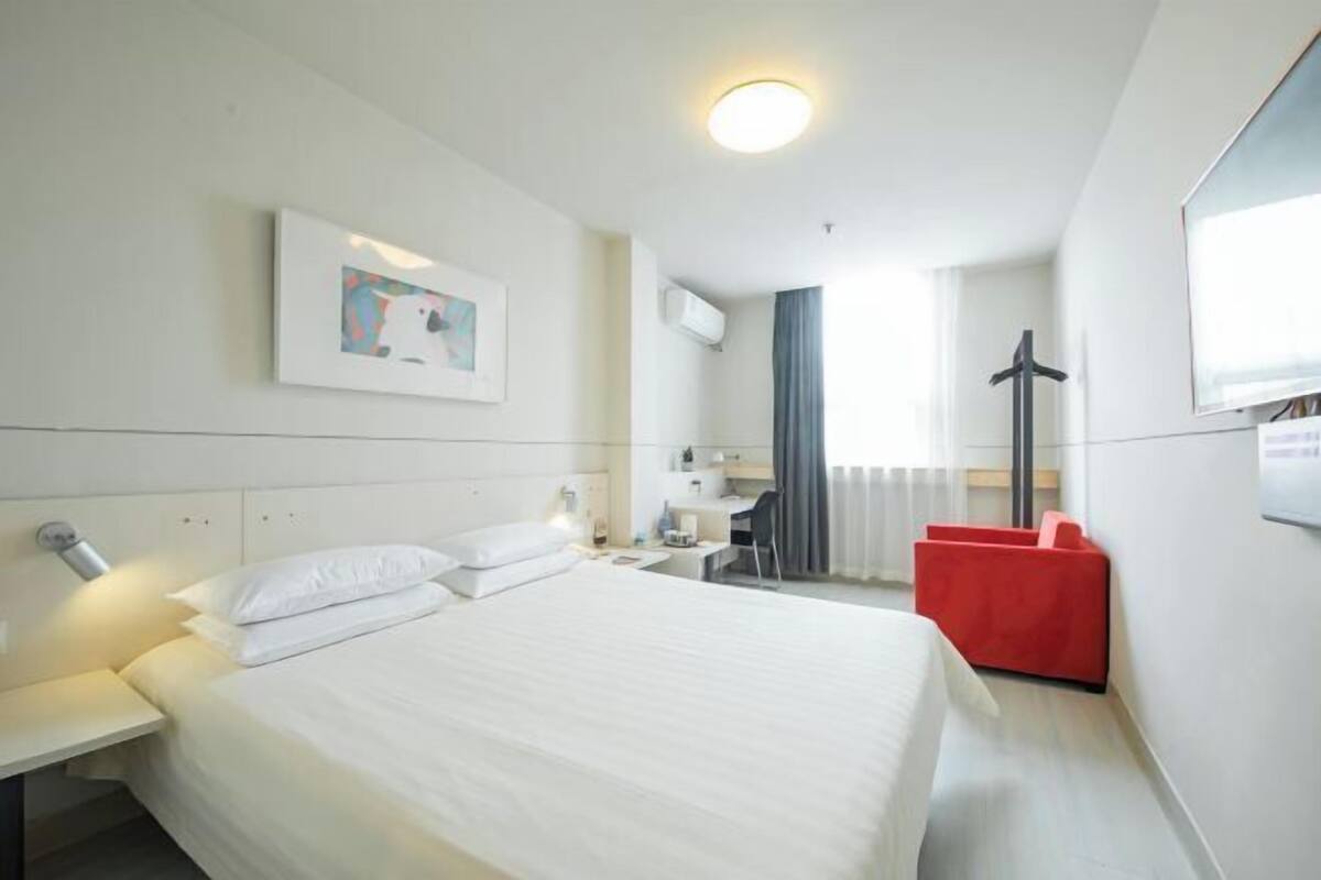 Habitación de hotel con una cama grande, un escritorio, una silla y una zona de estar roja.