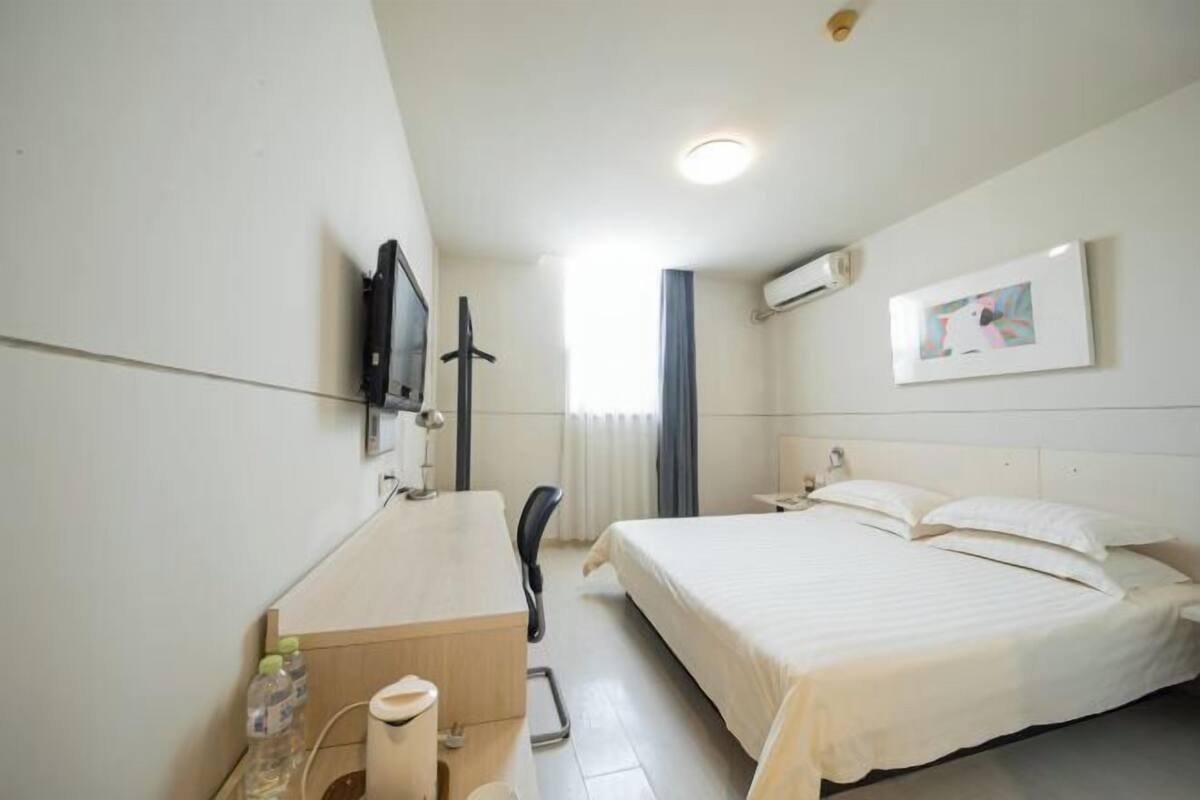 Habitación de hotel con cama, escritorio, silla, televisor y ventana con cortinas.