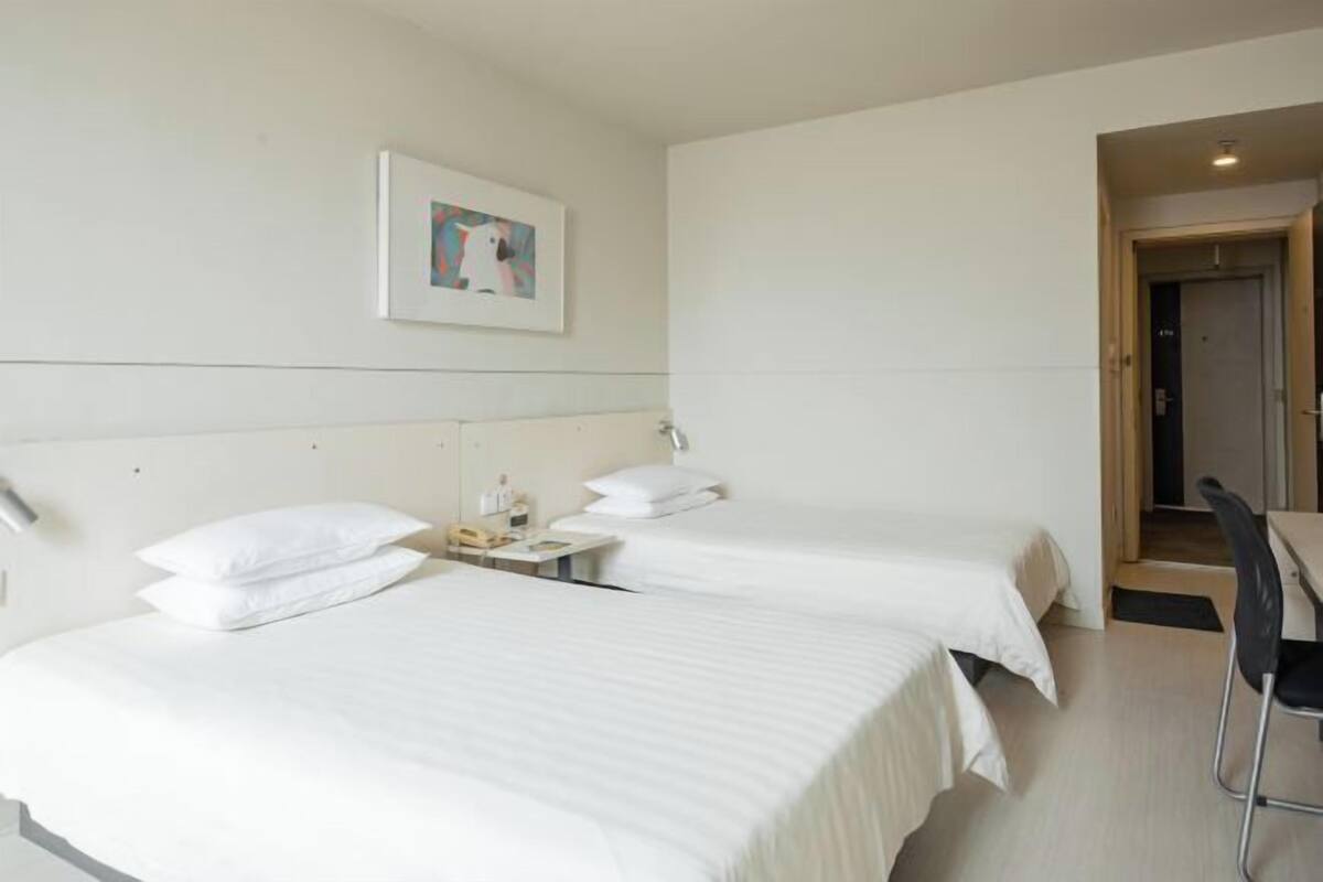 Habitación de hotel con dos camas, un escritorio, una silla y un cuadro en la pared.
