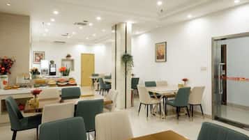 A hotel dining area with tables and chairs, a reception desk, and a large window.