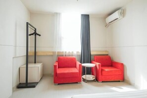 A small hotel room with two red armchairs, a small round table, a coat rack, a window with curtains, and an air conditioning unit. - Jinjiang Inn (LinyiWanxianghui Railway Station Hotel) (Linyi)