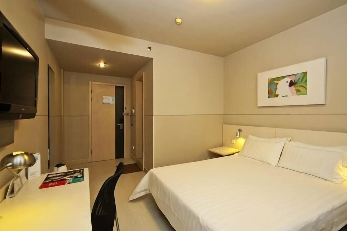 Una habitación de hotel con una cama, un escritorio con lámpara, un televisor y un cuadro en la pared.