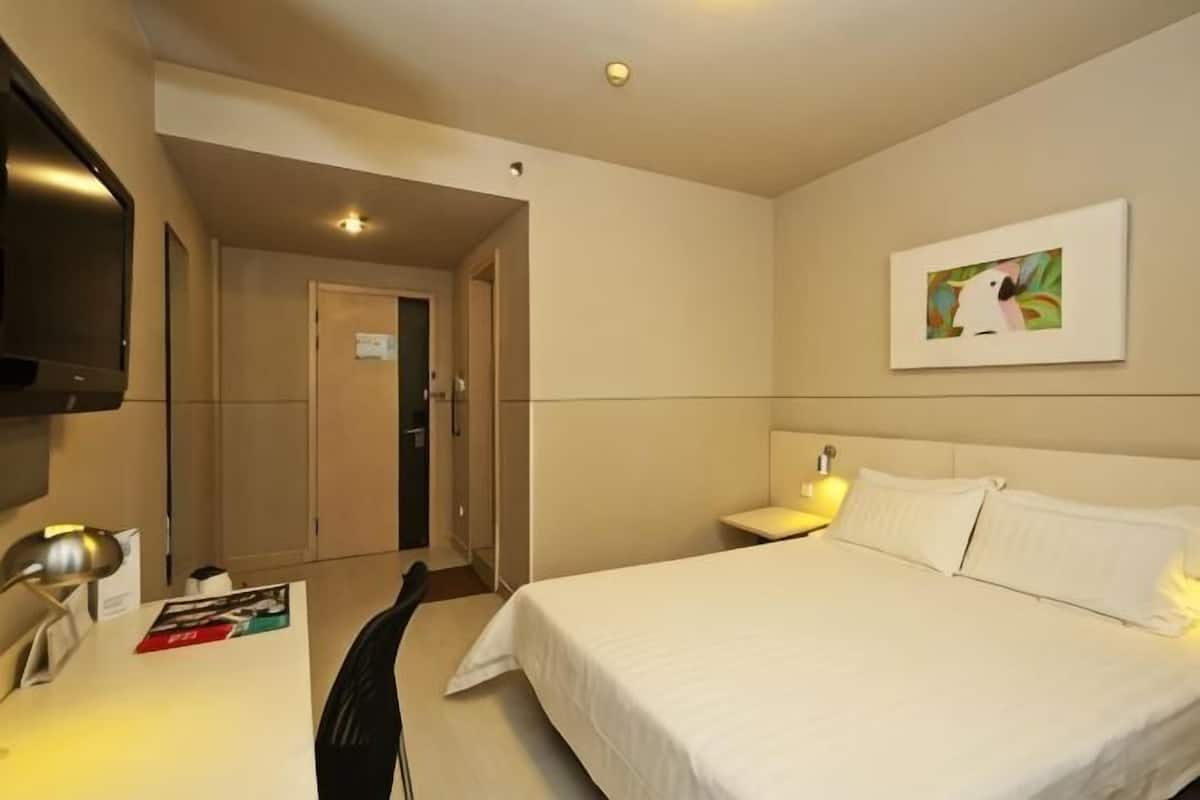 A hotel room with a bed, a desk with a lamp, a television, and a painting on the wall.