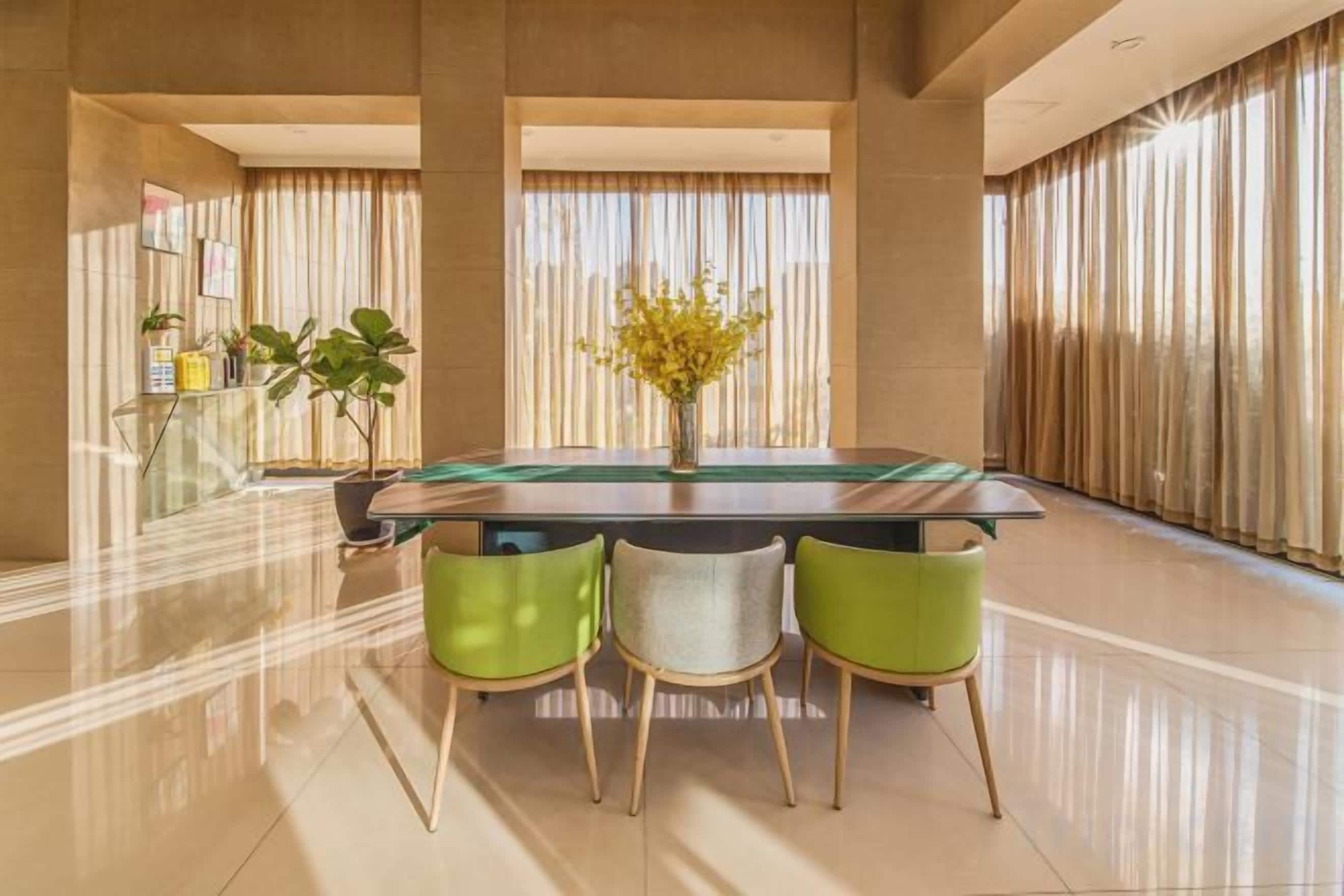 A modern dining area with a glass-top table, green chairs, and a vase of yellow flowers.