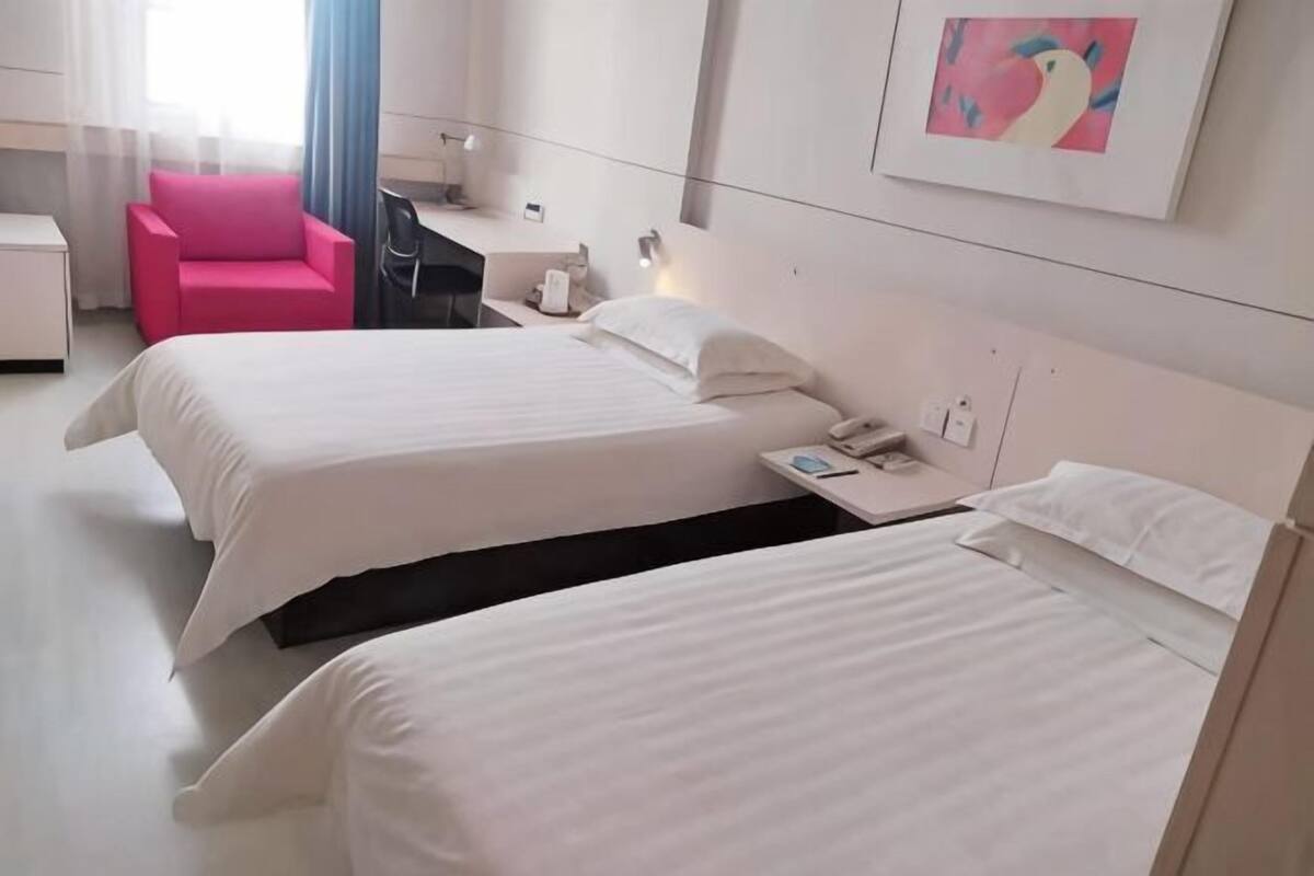 Habitación de hotel con dos camas, un escritorio, una silla, una lámpara de escritorio, un teléfono y un cuadro en la pared.