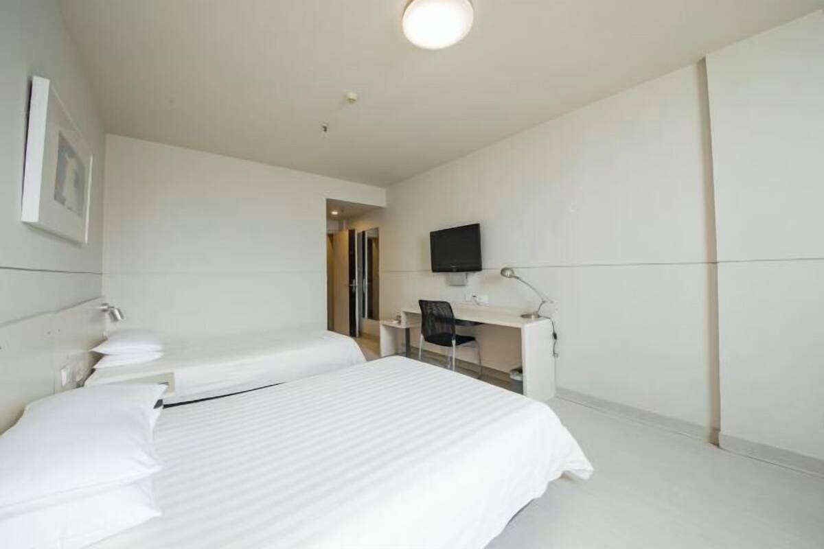Habitación de hotel con dos camas, un escritorio, una silla, un televisor de pantalla plana y un cuadro en la pared.